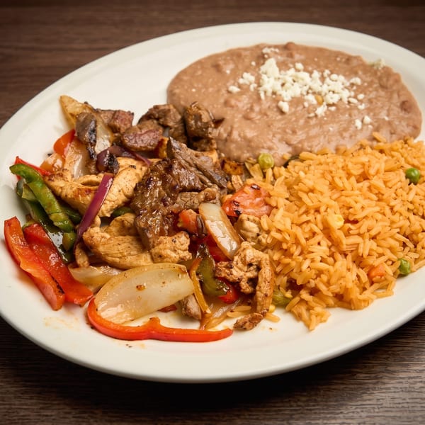 Chicken and beef fajitas with bell peppers and onions, served with rice and refried beans.