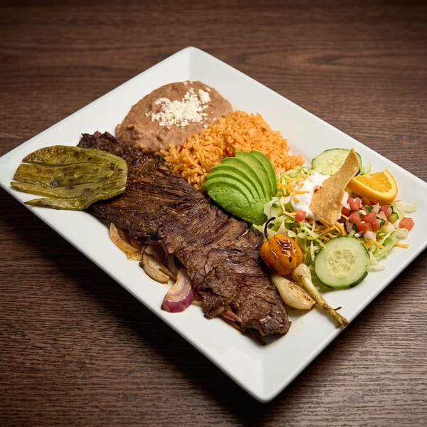 Grilled steak with refried beans, rice, avocado, salad, and grilled vegetables on a white plate.