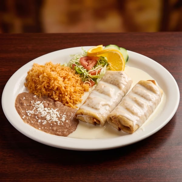 Two enchiladas topped with white sauce, served with rice, refried beans, and a side salad.