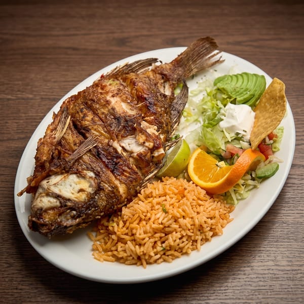 Whole fried fish with rice, salad, avocado, sour cream, lime, orange, and a tortilla chip.
